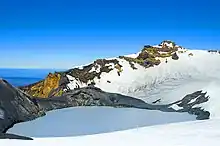 Frozen lake in the cradle of a snow-capped mountain with jagged rocky peaks