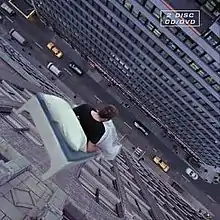 A person in a bed falling from a high floor of a multi-storey building to a road