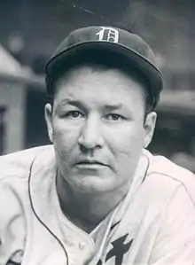 A man, wearing a baseball cap with the Detroit Tigers' Old English "D" logo in the center and a white baseball uniform with obscured lettering, faces forward.