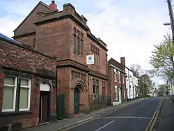 A two-storey building in sandstone with an arched doorway, and mullioned and transomed windows