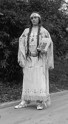 Ruth Muskrat, holding The Red Man In The United States (1919), by Gustavus Elmer Emmanuel Lindquist (1886-1967), on December 13, 1923. The book’s beaded cover and dress were made by an Indian woman of the Cheyenne tribe, Fish Woman. The book is an study of the social, religious, and economic life of American Indians, made under the auspices of the Institute of Social and Religious Research.