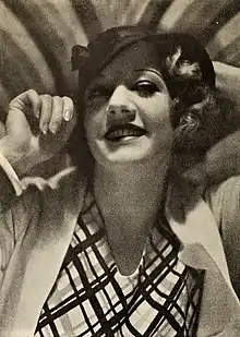 Ruth Selwyn, a smiling white woman with short blonde wavy hair, wearing a hat and a blouse with a graphic print