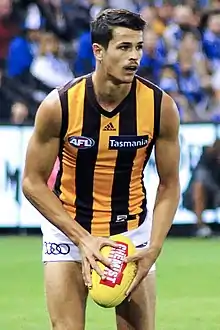 Male athlete in sleeveless guernsey holds football