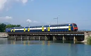 Blue locomotive pushing double-decker coaches across a bridge