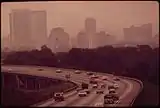 Cars travel over a highway overpass with the smog-obscured Birmingham skyline in the background