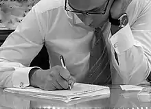 A man in a formal shirt and tie writes in a notebook