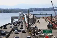 A bridge with a heavy amount of traffic and a bridge still under construction, with bare concrete and staging equipment, seen alongside each other.