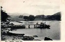 Passengers joining a small steamboat from a low pier