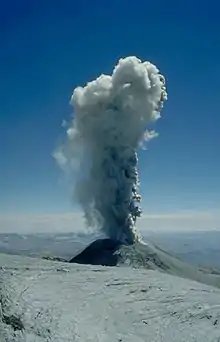 A large plume of smoke rising over a volcano which is slightly below the observer