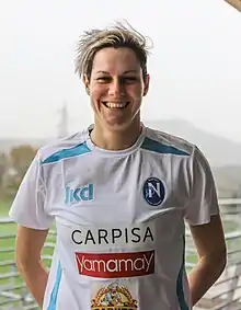 Headshot of a blonde-haired woman in a white football shirt.