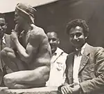 A young Sagini standing beside his statue of a nude man