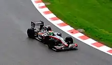 A black car with the name Sakon on the sidepods being driven on a wet track