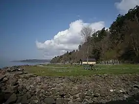 Picnic tables on a lawn surrounded by a steep rocky beach