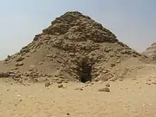 Ruined pyramid with a deep black depression at the center of the base of the pyramid.