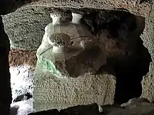 Image of a large stone sarcophagus viewed from above. The lid has four mushroom-like protrusions at each of the lid corners. The bottom right protrusion is broken. The sarcophagus lid has lengthwise striations.