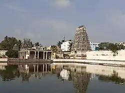 A lozenge-shaped tower tapering towards the top. It is covered in carvings including human figures and has an ornamental roof. It has a temple tank in the foreground