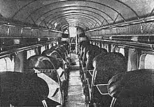 Grainy black-and-white image of single seats separated by the aisle, photographed from rear of plane facing cockpit