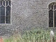 A section of the external north wall of the Chancel, between two Perpendicular period windows. The flints are laid in alternating rows at different angles, typical of Anglo-Saxon work known as herringbone pattern.