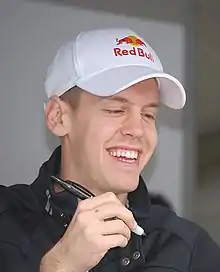 Sebastian Vettel signs an autograph while wearing a hat