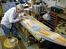 Man bending over a wooden, painted sculpture with a tool in his hand.