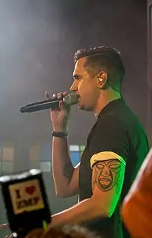 White male wearing short-sleeved shirt, holding a microphone, with earphones