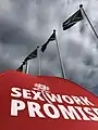 Image of a red umbrella with the words 'sex work promise' on it, against a backdrop of South African flags.