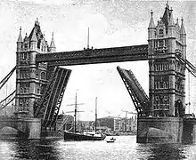 A ship with two tall masts is passing beneath the raised carriageways of a road bridge. The bridge has twin ornamental stone towers which are connected by a walkway high above the river.