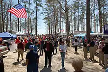 People stroll in a wooded area decorated with American flags.