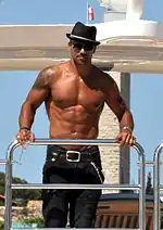 A shirtless man wearing a hat and jeans.