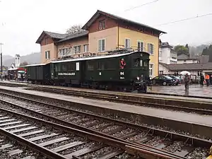 Boxy green railcar in front of three-story building