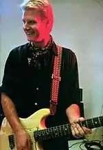 Smiling man, who is standing and playing guitar.