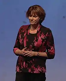 A Caucasian woman with brown hair holding her hands together while presenting