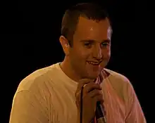 A man in a white T-shirt smiles and grasps a corded mic at its top
