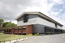 A large modern sporting complex adjacent to a grassed playing field.