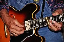 A musician playing a slide guitar with a slide on their little finger
