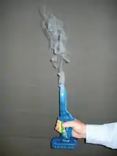 A hand grasping a small blue apparatus with white smoke emerging from its top
