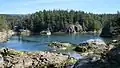 A small bay, with a boat docked at the far end and surrounded by tall pine trees