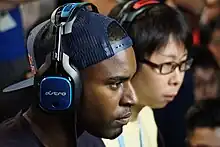 Two young men, Darryl Lewis and Goichi Kishida, sitting side-by-side, wearing headphones and focusing on their game.