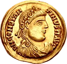 A gold coin showing the profile of a man with two strings of beads in his hair.