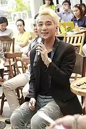Tùng, seated, holding a microphone
