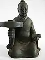 A candle stick holder depicting a man in a robe with a youren opening, Southern dynasty (420-589 AD).