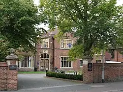 A two-storey brick building with stone windowframes, beyond a short, cobbled driveway.