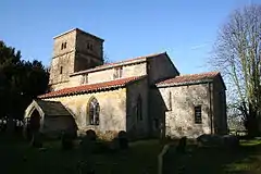 A stone church with a red tiled roof seen from the southeast, with a small chancel, a larger nave with clerestory and porch, and a tower
