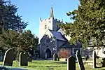 a church with a square tower and small spire, in a churchyard with trees and headstones
