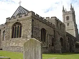 A headstone in front of a stone building with a square tower.