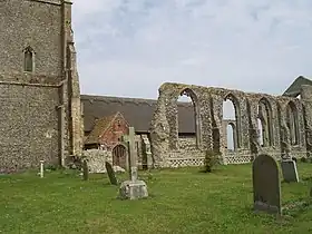 On the left the lower part of a tower, on the right the ruined wall of the aisle, and between them part of the small newer church with a thatched roof