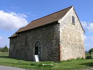 A simple stone church seen from the northeast with a tiled roof, a nave with a round-arched doorway and, beyond, a smaller chancel