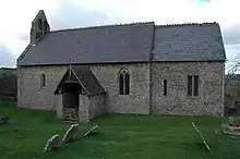 A small simple church seen from the south, with thin windows, a porch, a bellcote at the west end, and a short chancel