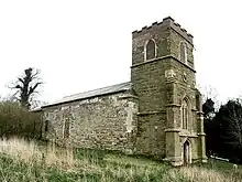 A stone church seen from the northwest. In the foreground is a battlemented tower with a west door and clock with the nave and chancel beyond.