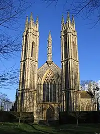 The west front of an elaborately designed stone church with slender twin towers, between which are a doorway, a large window and, at the top of the gable, a minaret-like pinnacle